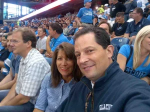 Dennis and his wife smiling at a Detroit Lions game with fans in the background.